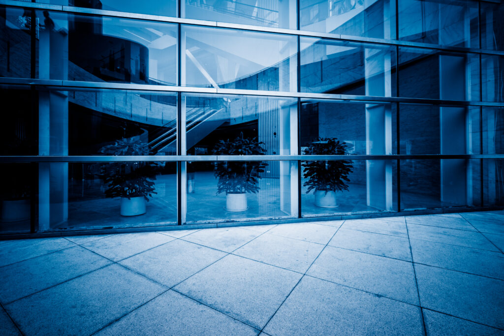 Blåtonad bild av en modern byggnad med stora fönster som visar en säker och välkomnande entré med gröna växter.