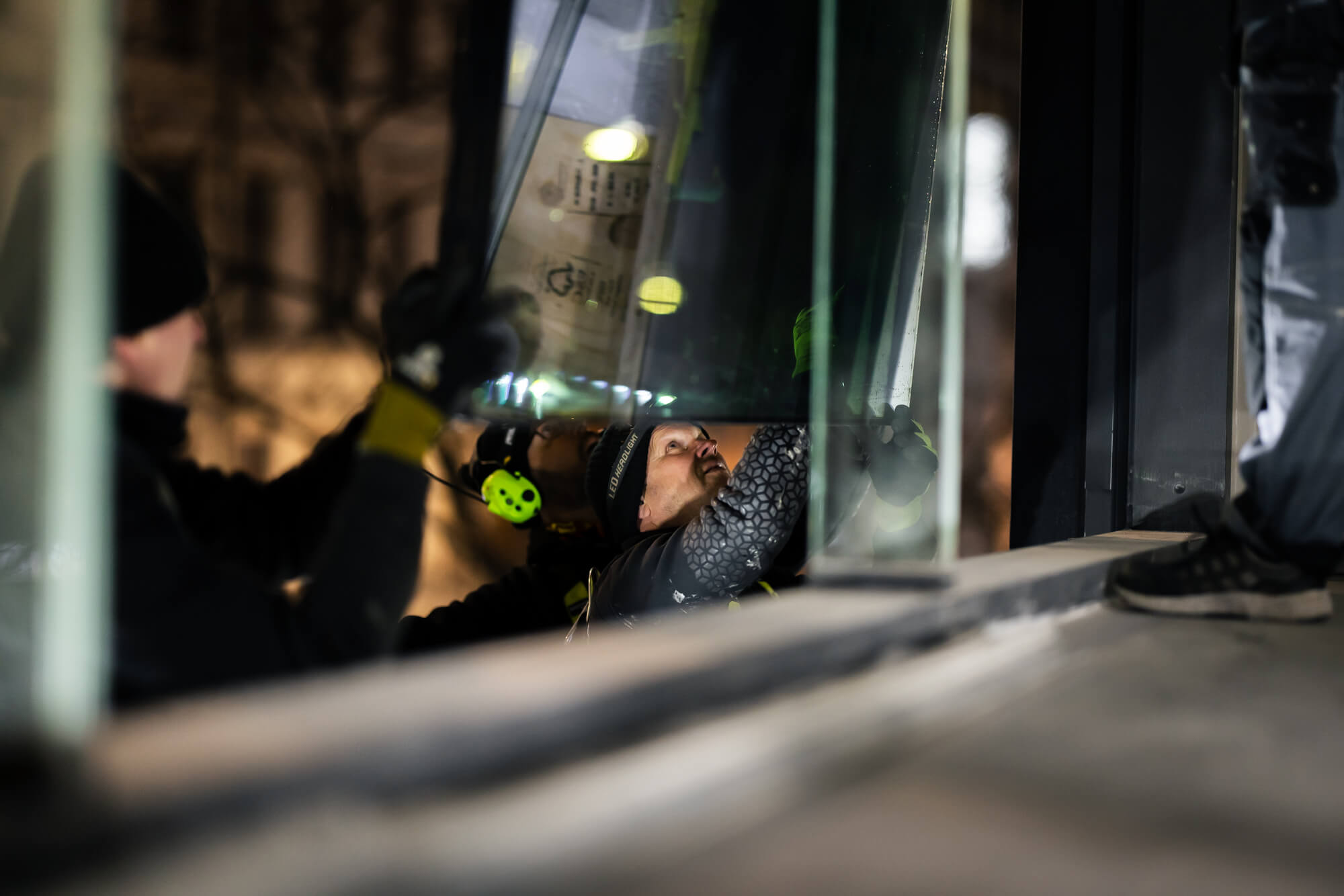 Närbild av tre Bollan-tekniker som koncentrerat installerar ett glasparti på kvällen med stadens ljus i bakgrunden.
